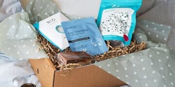 A relaxing gift box arranged on a bed with a magazine and treats