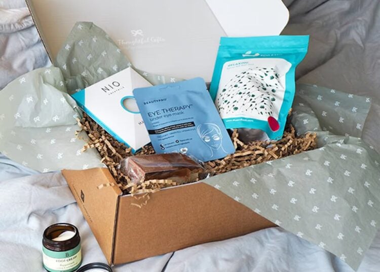 A relaxing gift box arranged on a bed with a magazine and treats