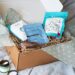 A relaxing gift box arranged on a bed with a magazine and treats