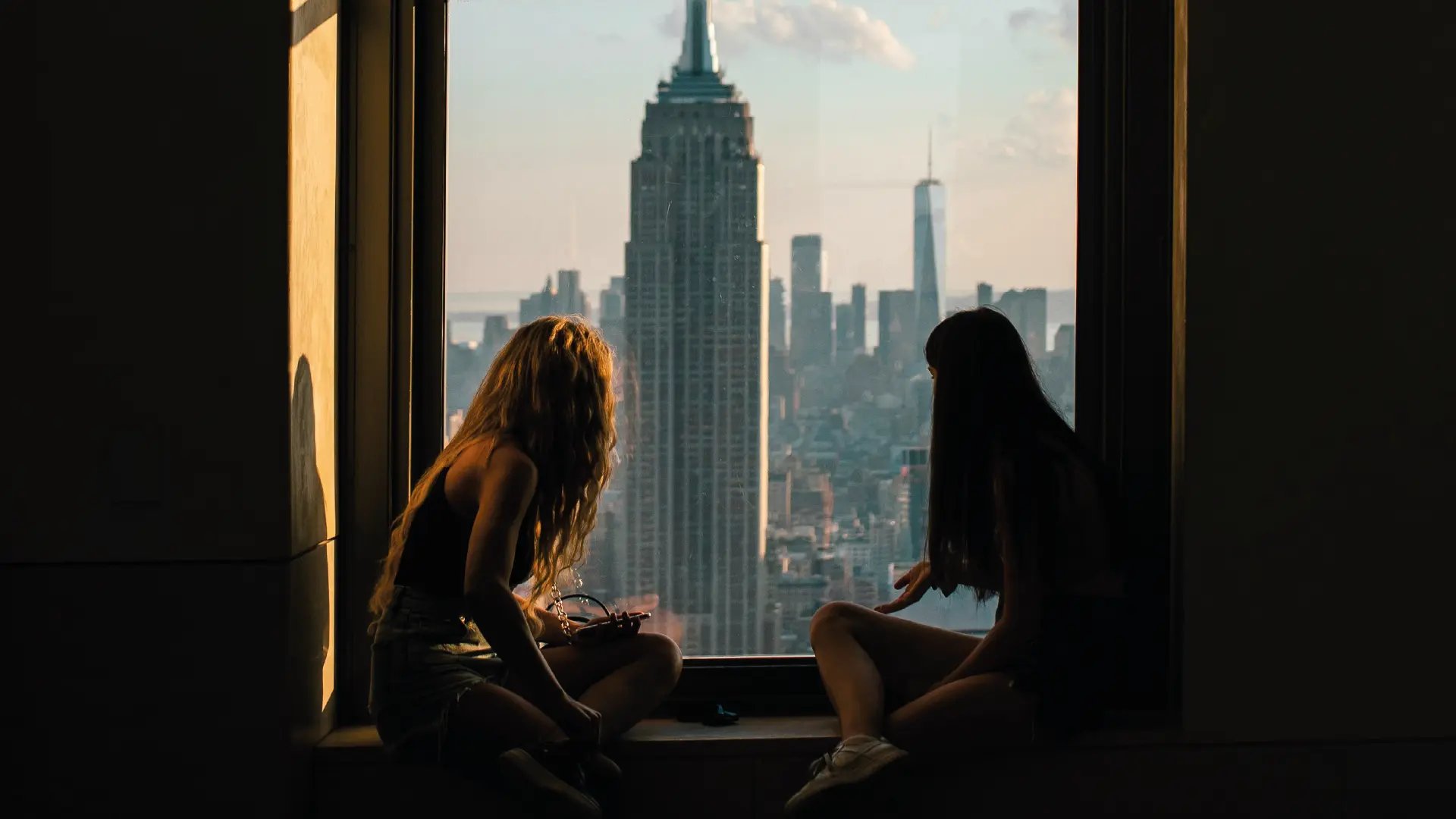 Dos mujeres junto a una ventana con vistas urbanas