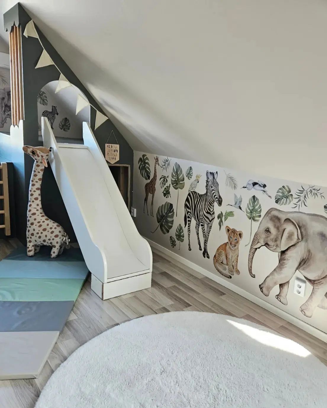 Childrens room with a white slide, jungle wall decor and a round rug