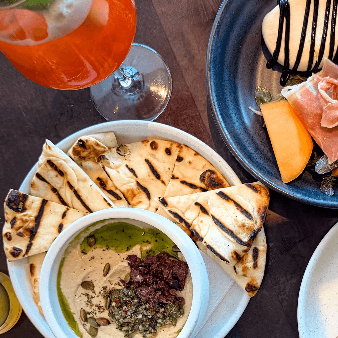ONE Dine dishes, flatbread and a bright cocktail arranged on a table