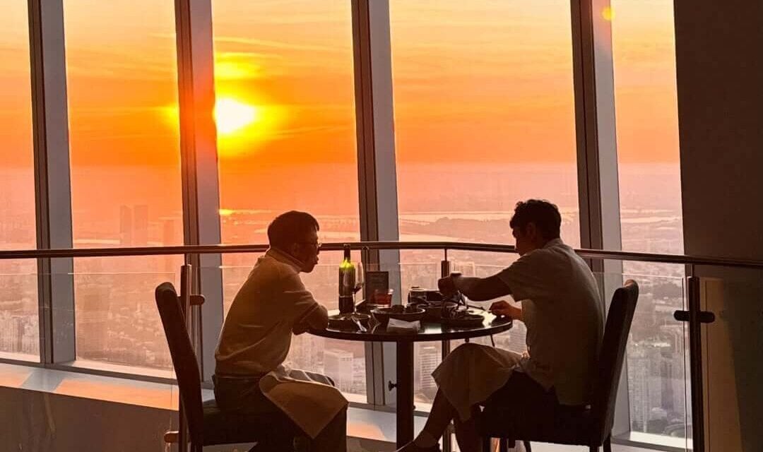 Two diners enjoying a sunset meal beside the windows at ONE Dine