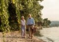 Mature couple strolling beside a river with a picnic basket
