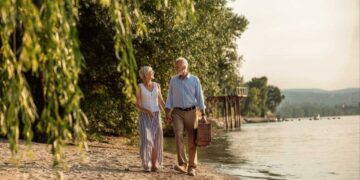 Mature couple strolling beside a river with a picnic basket