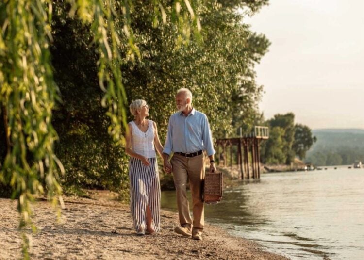 Mature couple strolling beside a river with a picnic basket
