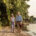 Mature couple strolling beside a river with a picnic basket