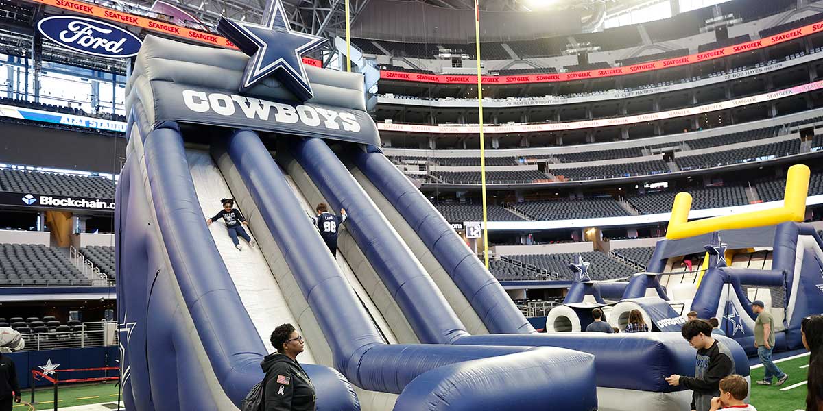 Families using a Dallas Cowboys inflatable slide on the AT&T Stadium field