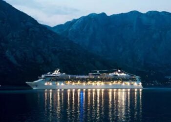 Cruise ship sailing at night with mountains behind it