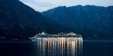 Cruise ship sailing at night with mountains behind it