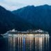 Cruise ship sailing at night with mountains behind it
