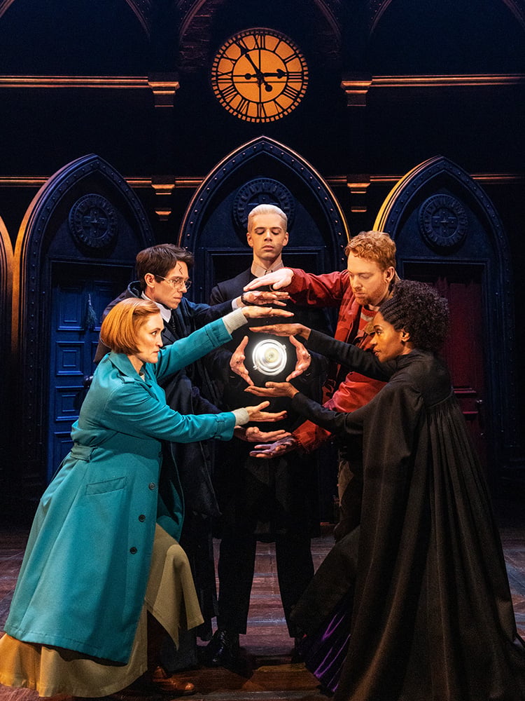 Five performers create a magical ritual beneath a glowing clock