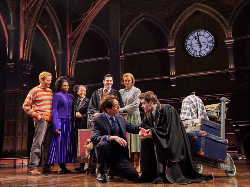 Broadway company gathered around trunks beneath the play’s clockwork stage set