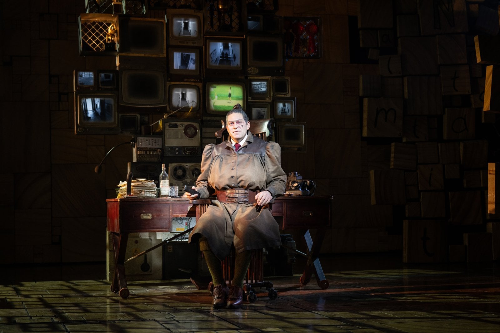 Trunchbull seated at a desk in Matilda The Musical