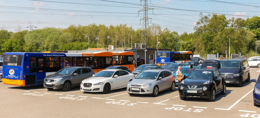 Airport parking shuttle buses beside parked cars