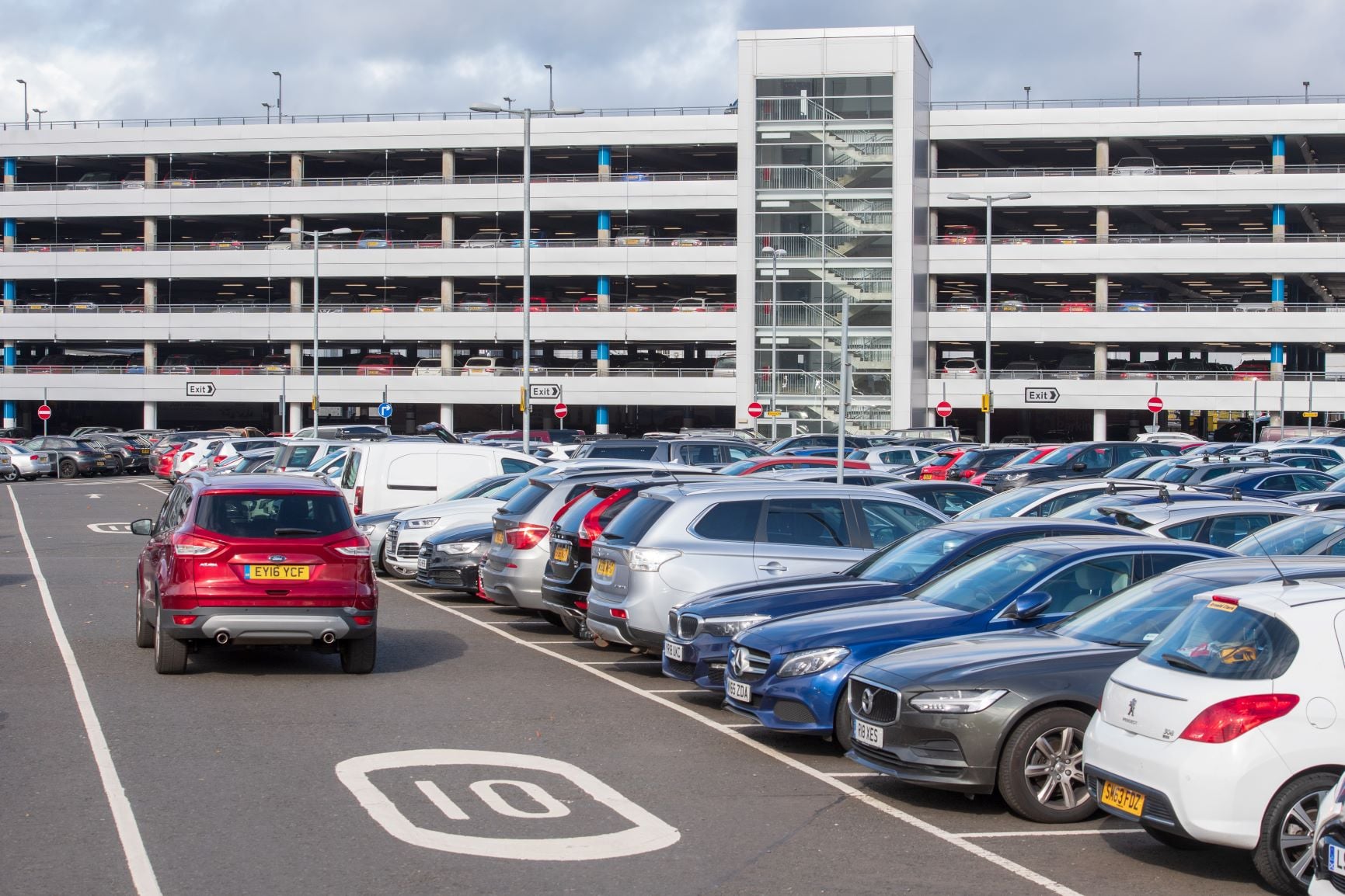 Cars parked in a surface lot beside an airport parking building