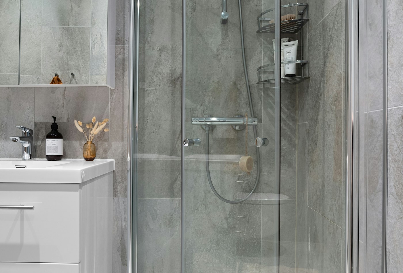 Grey stone bathroom with frameless walk-in shower beside a sink