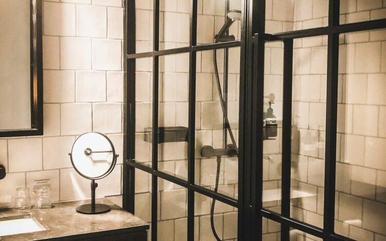 Hotel bathroom with a black-framed glass shower enclosure and white tiled walls