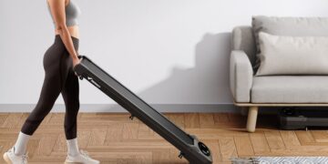A woman carries a Merach T26B1 treadmill through a bright living room