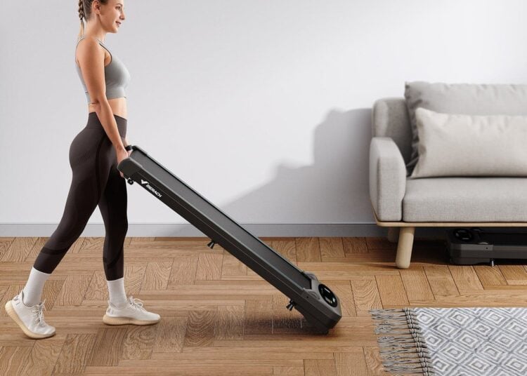 A woman carries a Merach T26B1 treadmill through a bright living room