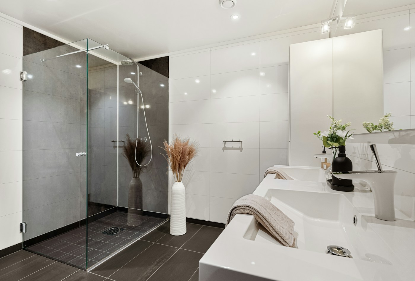 Minimal white bathroom with glass shower door and dark floor tiles