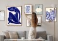 A person arranging framed art above a sofa in a living room