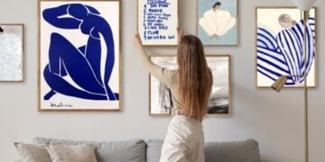 A person arranging framed art above a sofa in a living room