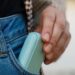 Una mano ripone IQOS ILUMA i nella tasca anteriore di jeans blu