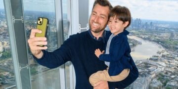 A parent and child take a selfie beside the windows overlooking London
