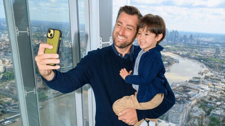 A parent and child take a selfie beside the windows overlooking London