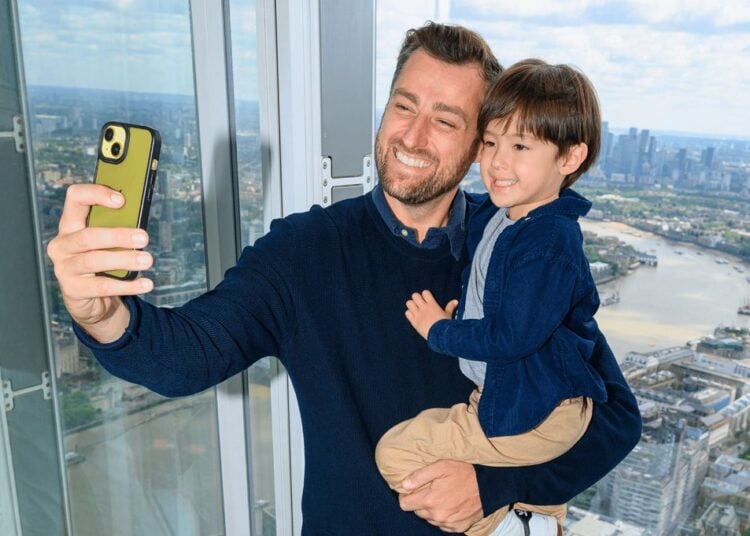 A parent and child take a selfie beside the windows overlooking London