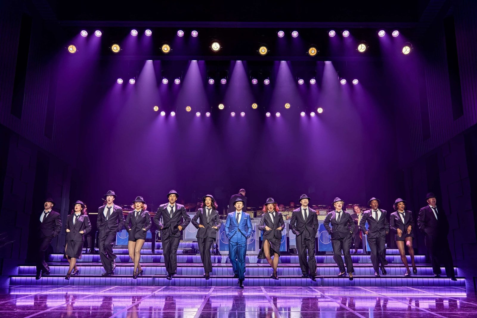 The cast performing together under purple stage lights