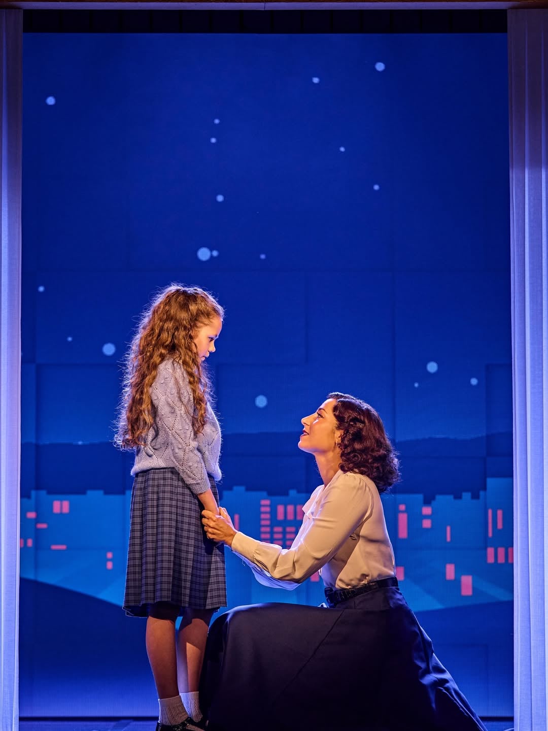 A woman speaking with a young girl in a scene from the musical
